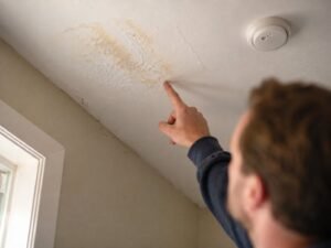 A person points to a faint water stain and bubbling paint on a white ceiling during a home showing.