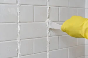 Thick white cleaning paste spread along the vertical grout lines of a white subway tile shower wall