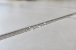 Three beads of water sitting on top of a light gray grout line without soaking in, showing the grout is sealed